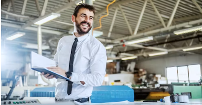 Photo d’un homme en chemise et cravate dans son 
                entreprise tenant son carnet ouvert et entrain de rire aux éclats en regardant au loin